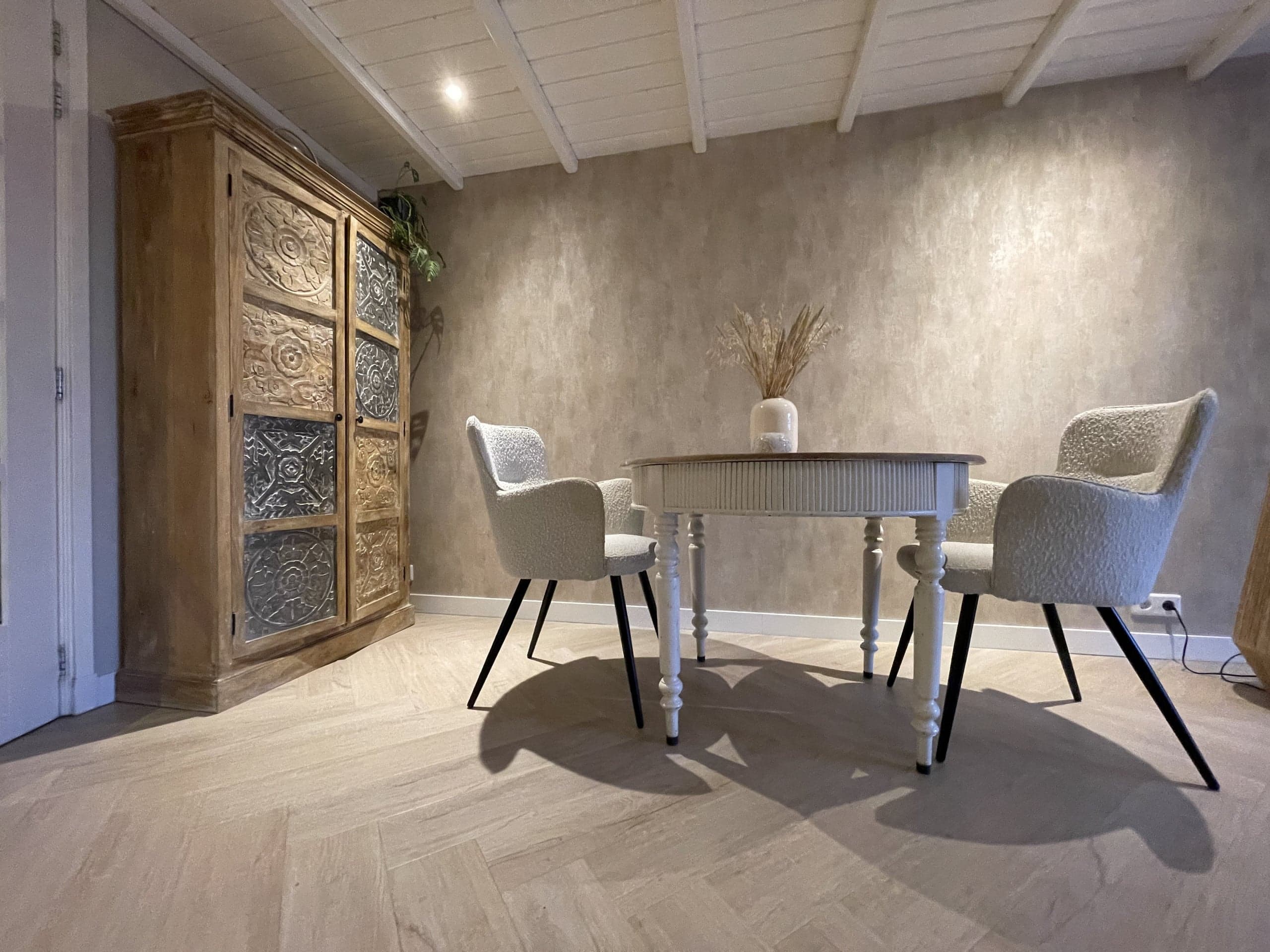 Ronde eettafel met vier stoelen en een houten kast in Oester